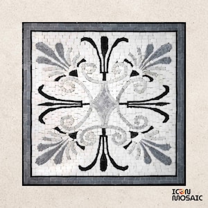 May include: Square mosaic tile with a symmetrical floral design in black, gray, and white. The central motif is a diamond shape, surrounded by stylized leaves and scrolls. The tile has a gray border and is set against a neutral background.