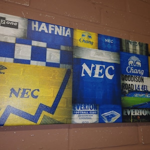 May include: A collage of blue and yellow fabric patches with various logos and text, including "NEC", "Everton Football Club", "Goodison Park", "Chang", "Hafnia", and "umbro".