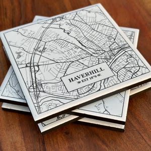May include: A stack of square coasters with a black and white map design. The coasters feature a detailed street map of Haverhill, with the text "HAVERHILL EST 1870" in a rectangular box. The coasters have black edges.