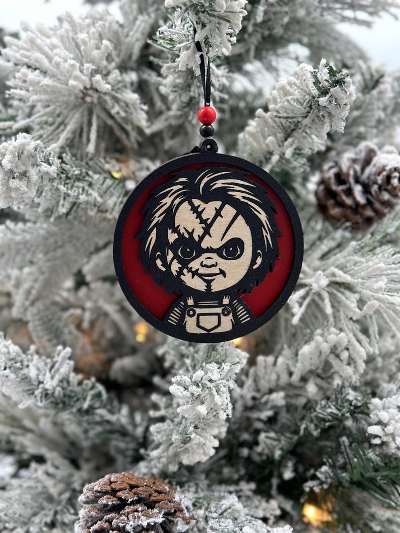 May include: A round wooden Christmas ornament featuring a black and white illustration of a character with a red background. The character has a stitched face and is wearing overalls.
