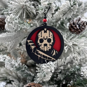 May include: A black and red round Christmas ornament featuring a silhouette of a hockey mask-wearing character holding a knife. The character's face is visible through the mask.