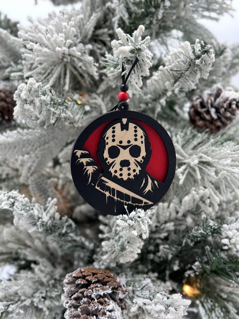 May include: A black and red round Christmas ornament featuring a silhouette of a hockey mask-wearing character holding a knife. The character's face is visible through the mask.