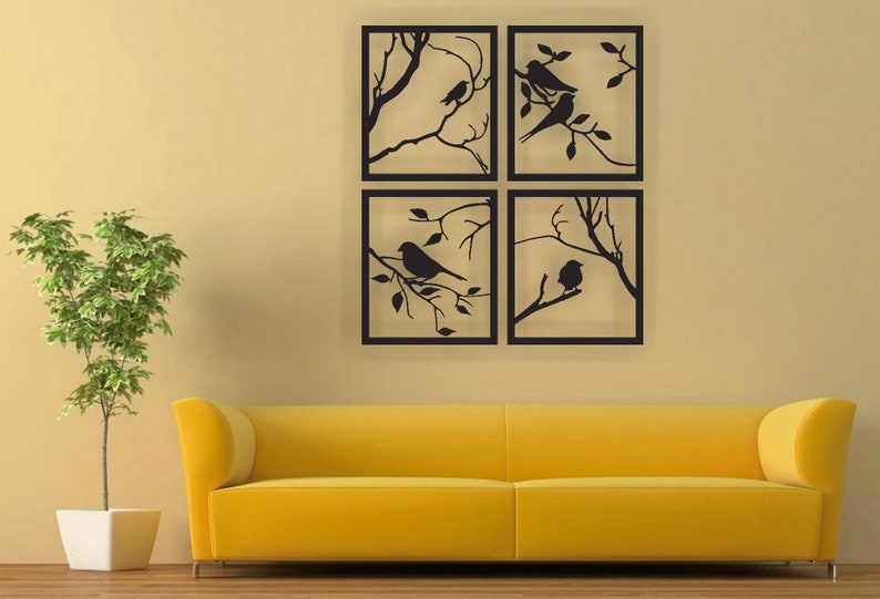 Op de afbeelding: Vier zwarte metalen lijstjes met wandkunst met silhouetten van vogels op takken. De lijstjes zijn in een vierkant gerangschikt en hangen aan een beige muur.