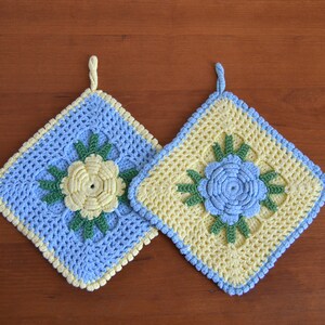 Könnte beinhalten: Zwei gehäkelte Topflappen mit Blumenmustern. Einer ist blau mit einer gelben Blume und der andere ist gelb mit einer blauen Blume.