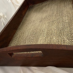 May include: A wooden serving tray with a gold-toned metal bottom. The bottom has a textured pattern of small circles. The tray has a curved handle on one side.