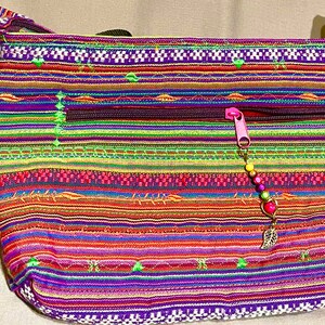 May include: A colourful striped fabric shoulder bag with a zipper closure and a beaded charm. The bag features a variety of colours, including purple, green, red, orange, and yellow.