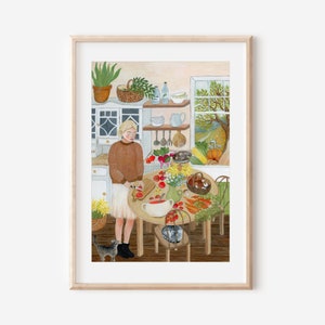 Op de afbeelding: Een ingelijste illustratie van een keukensc&egrave;ne met een persoon in een bruine trui en witte rok die tomaten snijdt op een houten plank aan een ronde tafel. Op de tafel staan groenten, een vaas met bloemen en een kom. Een kat staat op de vloer.