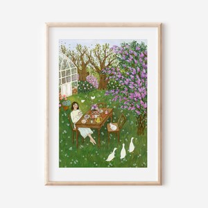 May include: A framed art print depicts a serene outdoor scene. A person sits at a table set for tea in a lush green garden, surrounded by flowering trees and white ducks. The artwork is in a light, airy style, with soft colors.