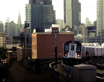 May include: A white subway train with a red circle on the front is pulling into a station. The train is in front of a brick building with a sign that reads "718-433-0077". There are tall buildings in the background.