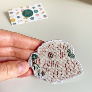 May include: White embroidered patch of a dog's face with pink and green details.