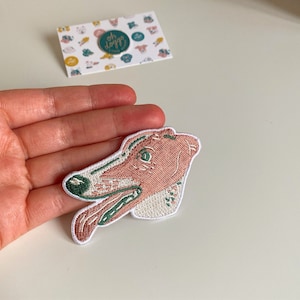 May include: A pink and green embroidered patch of a dog's head with its tongue sticking out.