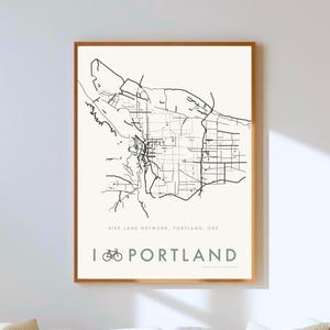 Peut inclure: Une affiche encadrée représentant une carte en noir et blanc du réseau de pistes cyclables de Portland, Oregon. L'affiche comprend le texte "I ⚀ PORTLAND" dans un design minimaliste. Le cadre est de couleur marron chaud.