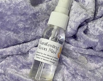 May include: A clear glass bottle with a white spray top, labeled "Manifesting Moon Mist" and "Blessed by the Moon & Citrine", with a blend of amber and sweet orange essential oils.