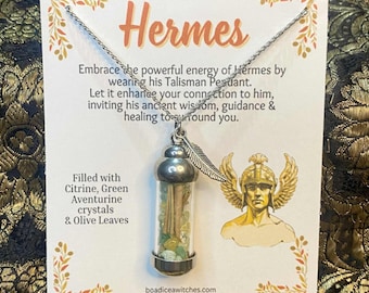 May include: A silver necklace featuring a glass vial pendant filled with citrine, green aventurine crystals, and olive leaves. The card displays the name "Hermes" and text about the pendant's properties.