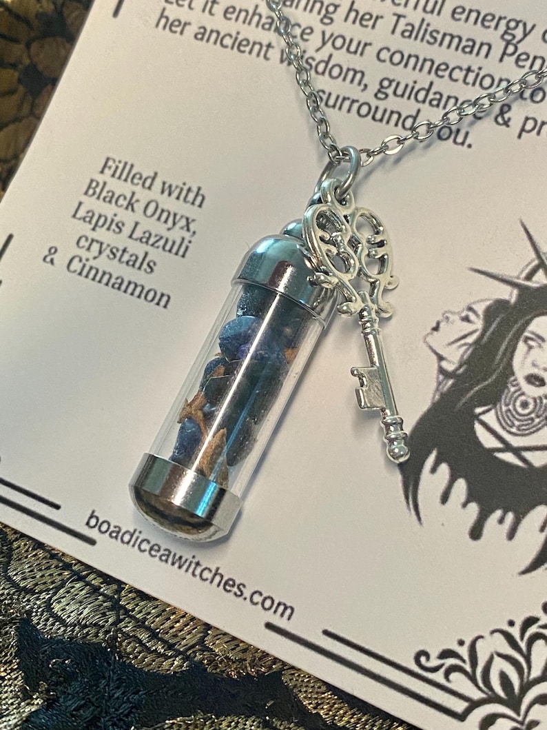 May include: A silver-toned necklace featuring a clear vial pendant filled with blue crystals and cinnamon sticks. A decorative key charm hangs next to the vial. The text on the card reads "Filled with Black Onyx, Lapis Lazuli crystals & Cinnamon."