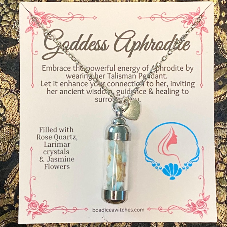 May include: A silver-toned necklace with a clear glass pendant filled with rose quartz, larimar crystals, and jasmine flowers. The card behind the necklace reads "Goddess Aphrodite" and includes text about the pendant's energy.