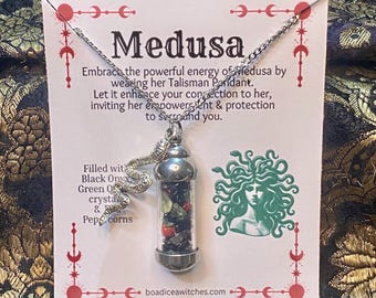 Puede incluir: Collar plateado con un colgante de vial de vidrio. El vial contiene ónix negro, cristales verdes y granos de pimienta. La tarjeta detrás del collar presenta la palabra "Medusa" y una ilustración verde de Medusa.
