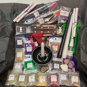 May include: A selection of spiritual items, including incense sticks, candles, herbs, crystals, and a smudge mist spray. The items are packaged in clear bags and small bottles, with a black bowl and a wooden incense holder. The overall color scheme is a mix of natural tones and vibrant colours.