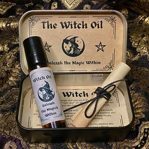 May include: An open metal tin with a Witch Oil roller bottle, a scroll, and printed cards. The bottle is labelled "Witch Oil" and "Unleash the Magick Within." The tin lid features the text "The Witch Oil" and a witch illustration.