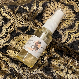 May include: A clear glass bottle with a white spray top and a white label that says "Goddess Mist Lilith Spray". The label has a black and red illustration of a woman with wings.
