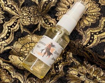 May include: A clear glass bottle with a white spray top and a white label that says "Goddess Mist Lilith Spray". The label has a black and red illustration of a woman with wings.