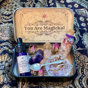 Peut inclure: Une boîte en métal contenant un flacon compte-gouttes en verre bleu étiqueté Lotus Moon Oil, un petit flacon en verre bouché avec des cristaux roses, un plus grand flacon avec des fleurs séchées et cristaux, une pierre violette et une cuillère.