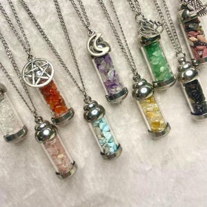 May include: A collection of silver-toned necklaces, each featuring a small glass vial filled with colorful gemstones. The vials are capped with silver metal and hang from delicate chains. Various gemstones include red, purple, green, and yellow.