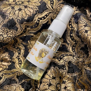 May include: A clear glass bottle with a white spray top and a white label. The label features a drawing of a woman's face with a laurel wreath and the text "Deity Mist Spray".