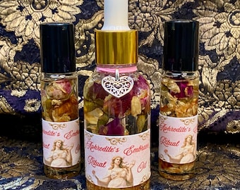 Può includere: Tre flaconi in vetro trasparente contenenti olio e petali di rosa essiccati. Il flacone centrale ha un contagocce bianco, un colletto dorato e un ciondolo a forma di cuore argentato. Ogni etichetta riporta il testo Aphrodite's Embrace Ritual Oil.