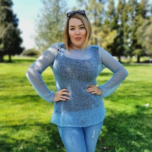 Puede incluir: Un suéter de punto azul claro, holgado, con un diseño transparente de tejido abierto. El suéter tiene mangas largas y un cuello redondo.