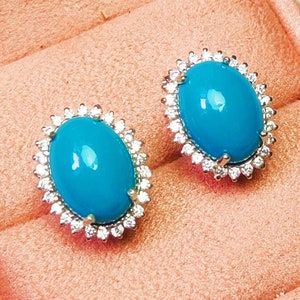 May include: A pair of turquoise oval earrings with a diamond halo setting. The earrings are displayed in a peach-coloured velvet box.
