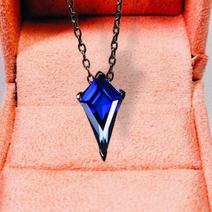 May include: A blue gemstone pendant necklace in a pink velvet jewelry box. The pendant is a pointed, faceted, geometric shape.