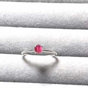 Pode incluir: Um anel de prata com uma pequena gema redonda rosa engastada no centro.