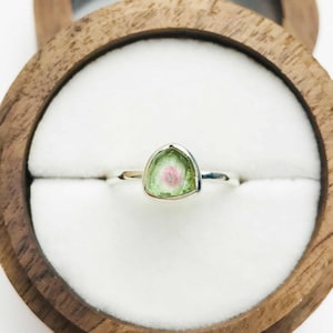 Può includere: Un anello d'argento con una pietra preziosa triangolare verde e rosa incastonata al centro.