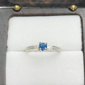 Peut inclure: Une bague en argent avec une pierre précieuse bleue sertie au centre. La bande de la bague a une finition texturée.