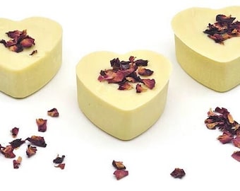 Puede incluir: Tres jabones en forma de corazón con pétalos de rosa secos en la parte superior. Los jabones son blancos y los pétalos son de color rosa intenso.