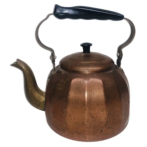 May include: A copper-colored tea kettle with a black handle and lid knob. The spout is a brass color, and the handle is made of metal. The kettle has a round body with a faceted design.