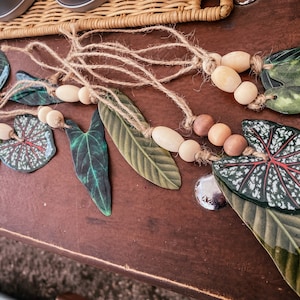 May include: A garland of green and white leaves with wooden beads strung on twine. The leaves are painted to look like real plants.