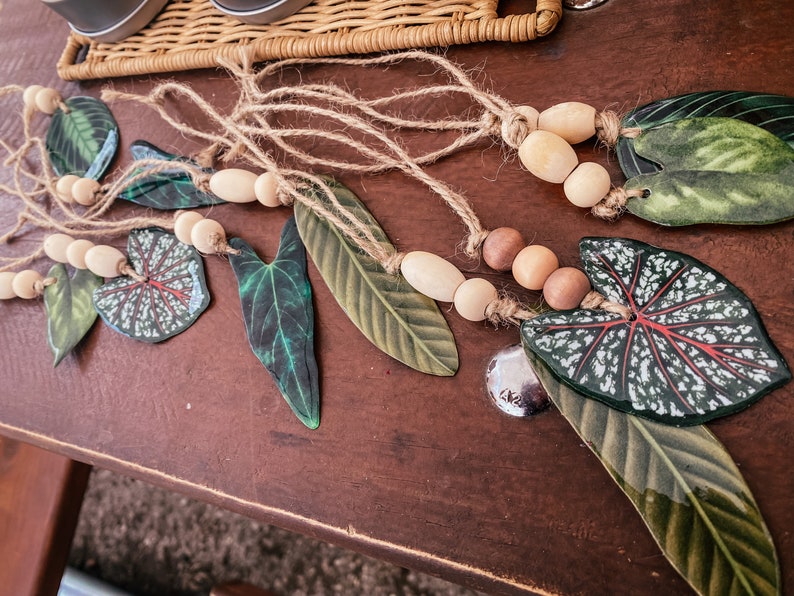 May include: A garland of green and white leaves with wooden beads strung on twine. The leaves are painted to look like real plants.