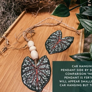 May include: Two leaf-shaped pendants, one for a car hanging and one for an earring, both with a white and green pattern and red veins. The car hanging pendant has wooden beads on a string.