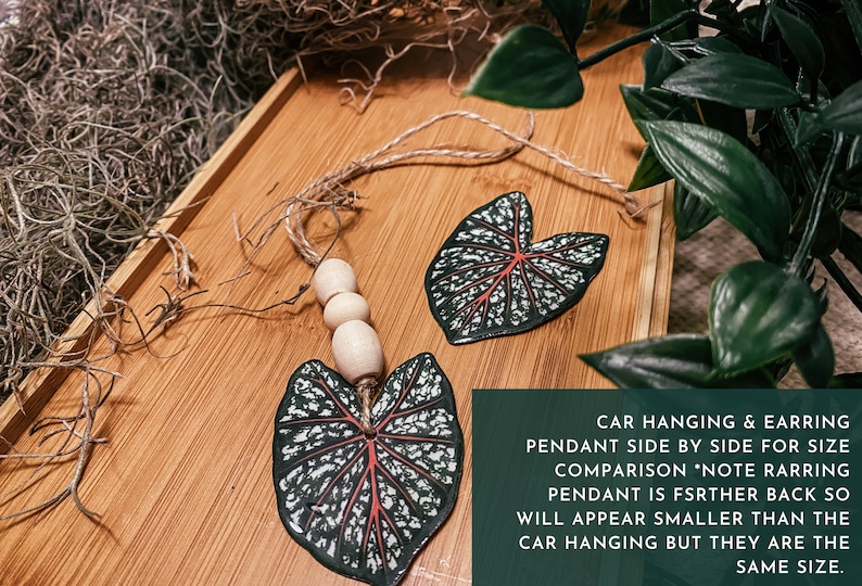May include: Two leaf-shaped pendants, one for a car hanging and one for an earring, both with a white and green pattern and red veins. The car hanging pendant has wooden beads on a string.