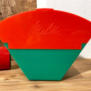 Peut inclure: Un filtre à café en plastique rouge et vert avec le mot "Melitta" imprimé sur le dessus.