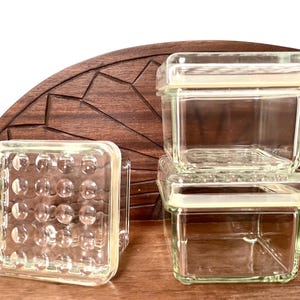 Set di 3 contenitori in vetro IKEA KOLONI con superficie irregolare, forma quadrata e coperchi con guarnizione in gomma.