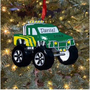 May include: Green monster truck Christmas ornament with a white background and the name "Daniel" and the year "2023" written on it.