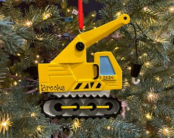 May include: Yellow construction crane Christmas ornament with black details, a black hook, and the name "Brooks" and the year "2024" written on it.