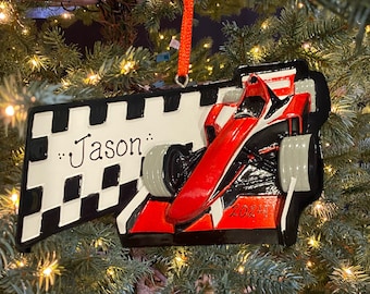 May include: A red and black race car Christmas ornament with a checkered flag background. The ornament has the name "Jason..." written on the flag. The car has the number "2024" on the side.