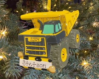 May include: Yellow and black dump truck Christmas ornament with the year 2024 and the name Stetson on the front.
