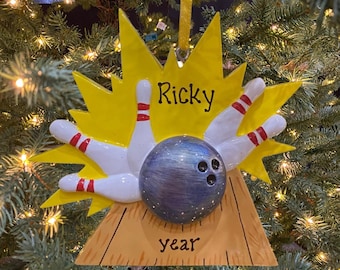 May include: Yellow and white bowling pin Christmas ornament with a blue bowling ball and the name "Ricky" and the word "year" on the base.