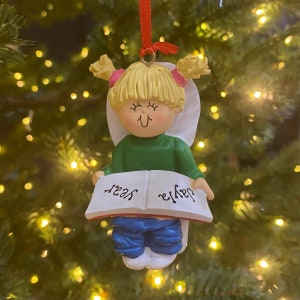 May include: A white porcelain Christmas ornament depicting a girl with blonde hair sitting on a toilet and reading a book. The book says "Daddy" on one side and "Yes" on the other.