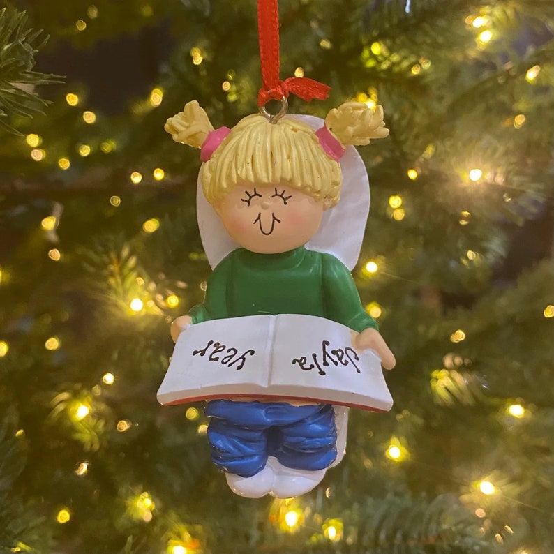 May include: A white porcelain Christmas ornament depicting a girl with blonde hair sitting on a toilet and reading a book. The book says "Daddy" on one side and "Yes" on the other.